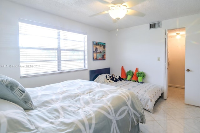 tiled bedroom with ceiling fan and a textured ceiling