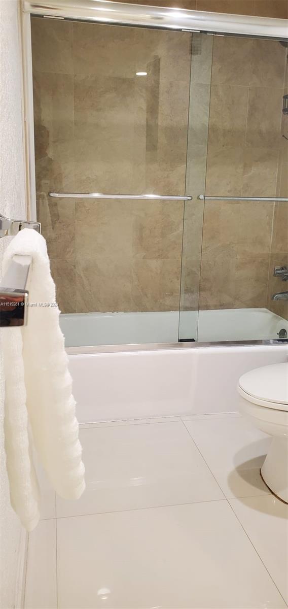 bathroom featuring combined bath / shower with glass door, tile floors, and toilet