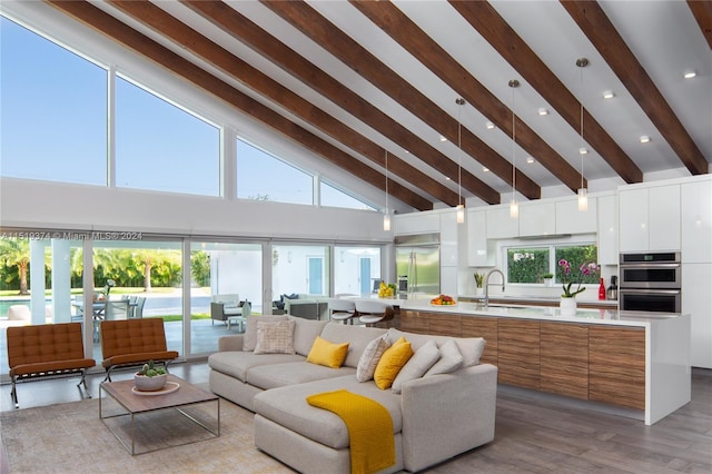 living room featuring beam ceiling, light hardwood / wood-style floors, high vaulted ceiling, and sink