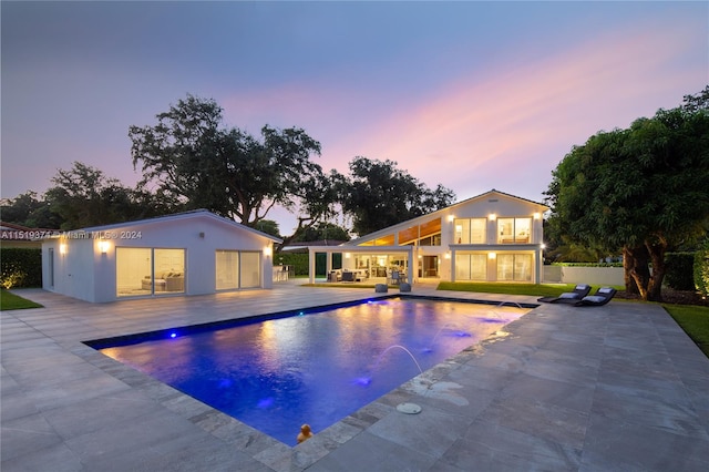 pool at dusk with a patio and pool water feature
