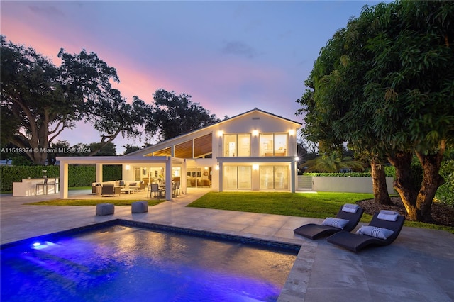 pool at dusk with a lawn and a patio area