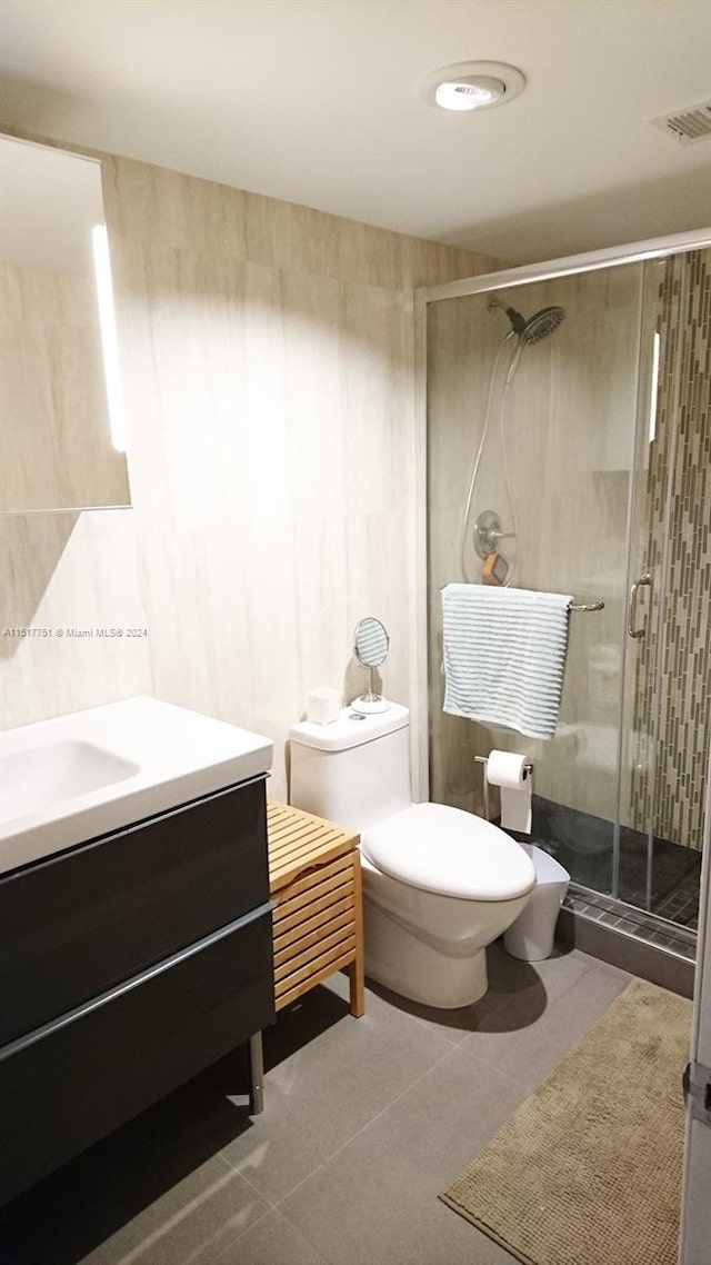 bathroom with toilet, vanity, a shower with shower door, and tile flooring