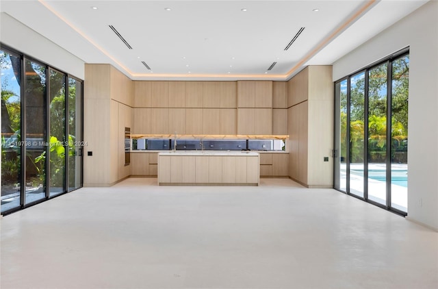 kitchen with a healthy amount of sunlight, concrete floors, light brown cabinetry, modern cabinets, and a center island