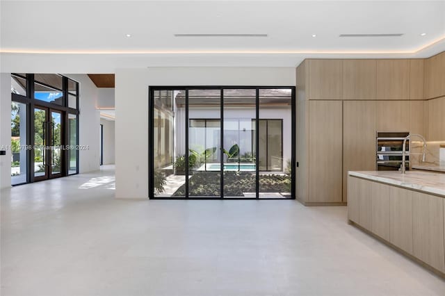 kitchen with modern cabinets, light brown cabinets, open floor plan, double oven, and light stone countertops