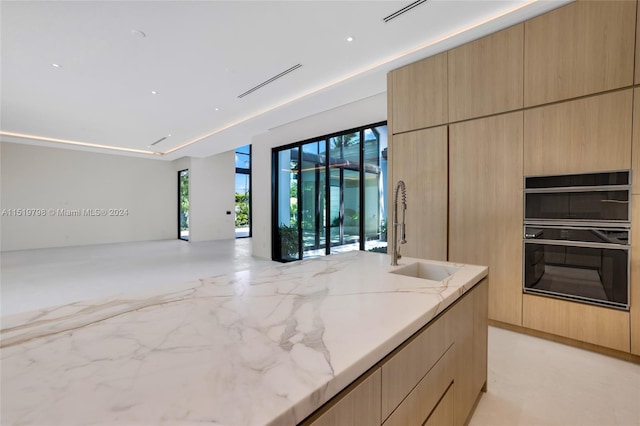 kitchen featuring light brown cabinets, light stone countertops, modern cabinets, dobule oven black, and a sink