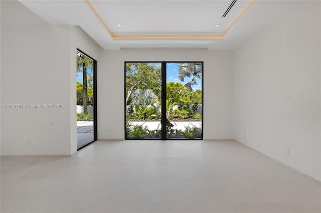 unfurnished room with a tray ceiling, a wealth of natural light, and finished concrete floors