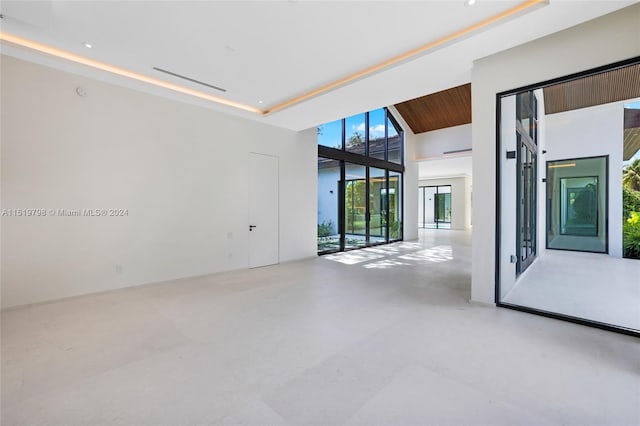 unfurnished room with a tray ceiling, a high ceiling, wooden ceiling, and concrete flooring