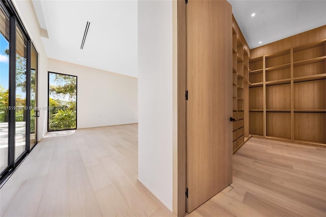 hall with recessed lighting, built in shelves, light wood-style floors, and a towering ceiling