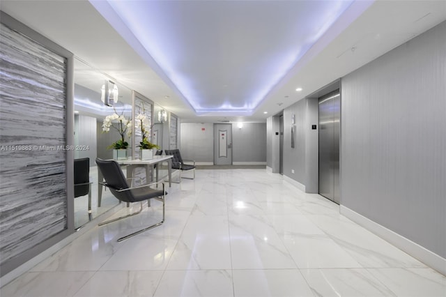 interior space with a tray ceiling, light tile floors, and elevator