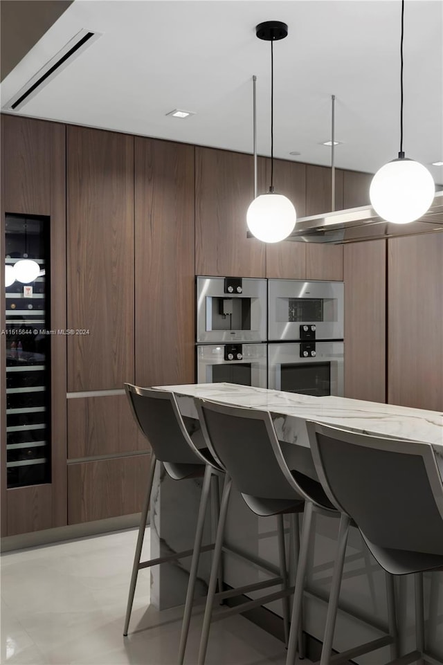 kitchen with stainless steel double oven, a kitchen breakfast bar, decorative light fixtures, and beverage cooler