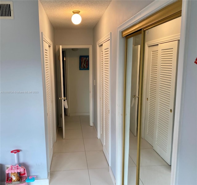 hallway featuring visible vents, a textured ceiling, and light tile patterned flooring