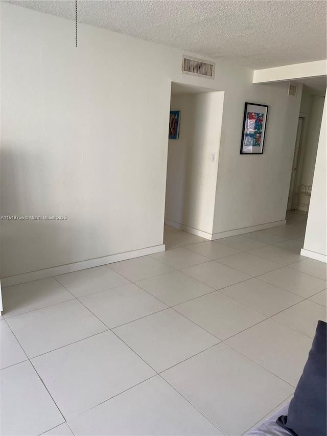 unfurnished room with visible vents, a textured ceiling, baseboards, and light tile patterned floors