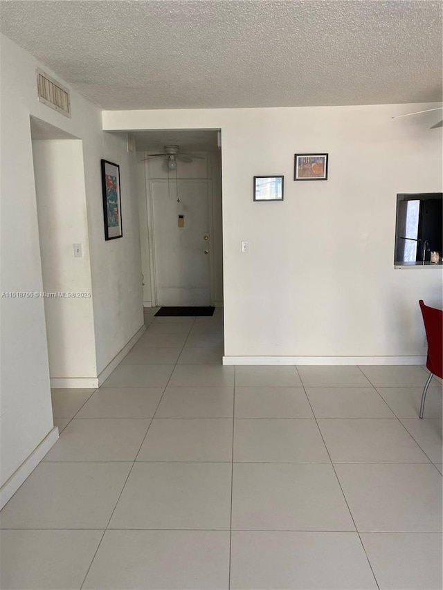 hall featuring visible vents, a textured ceiling, and light tile patterned flooring