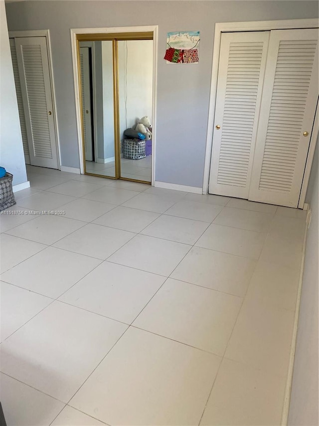 unfurnished bedroom with light tile patterned floors, two closets, and baseboards