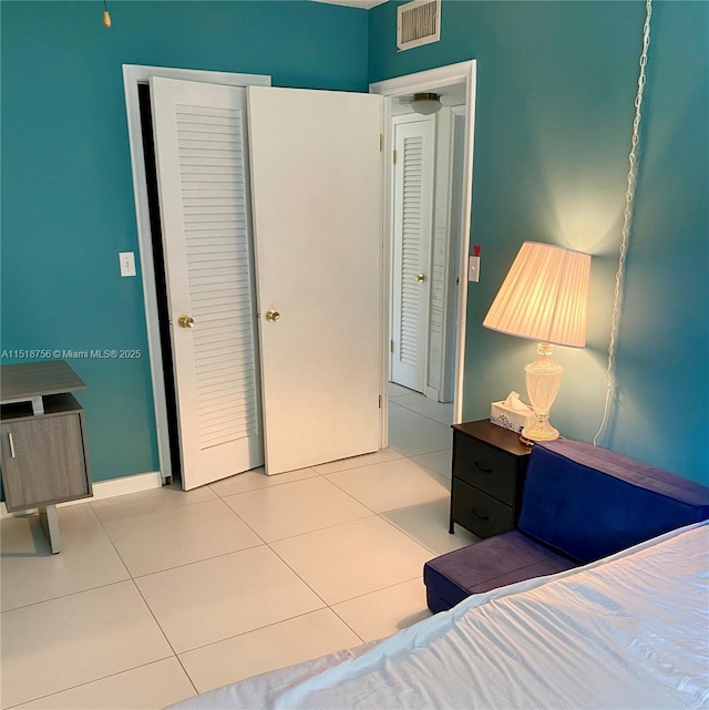 bedroom with light tile patterned floors, baseboards, visible vents, and a closet