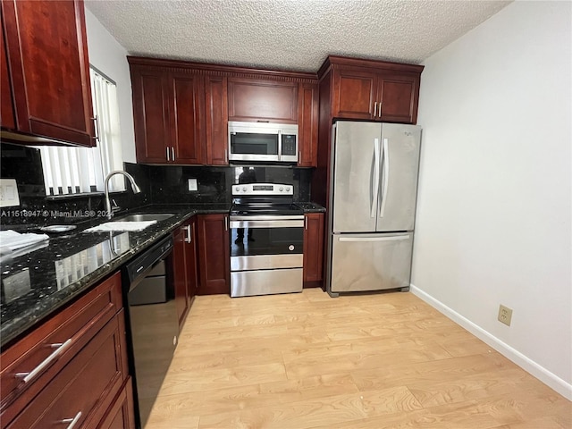 kitchen featuring sink, light wood-type flooring, dark stone countertops, stainless steel appliances, and tasteful backsplash