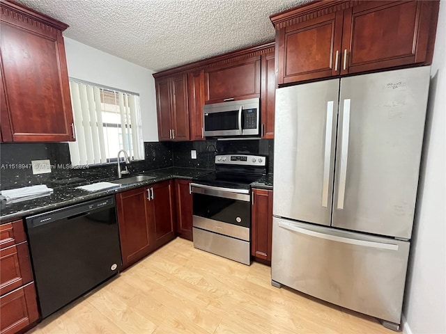 kitchen with light hardwood / wood-style flooring, appliances with stainless steel finishes, backsplash, dark stone countertops, and sink