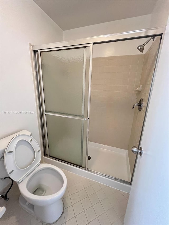 bathroom featuring toilet, a shower with door, and tile flooring