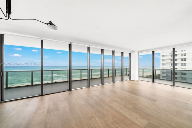 spare room with a water view, expansive windows, and light hardwood / wood-style floors