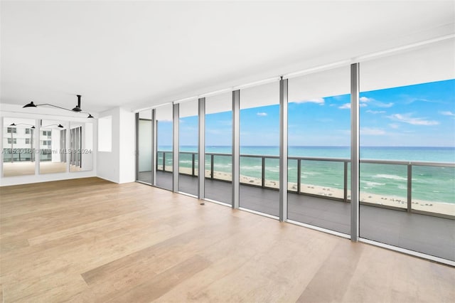 spare room featuring light hardwood / wood-style flooring, a view of the beach, floor to ceiling windows, and a water view