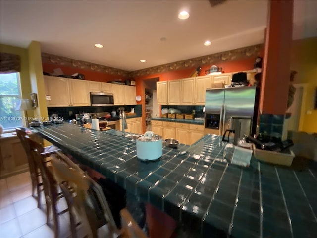 kitchen with a kitchen bar, tasteful backsplash, tile counters, appliances with stainless steel finishes, and tile floors