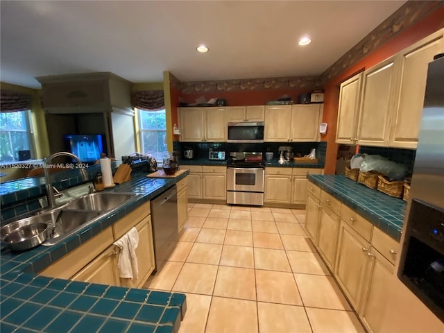 kitchen with stainless steel appliances, light tile floors, backsplash, tile countertops, and sink