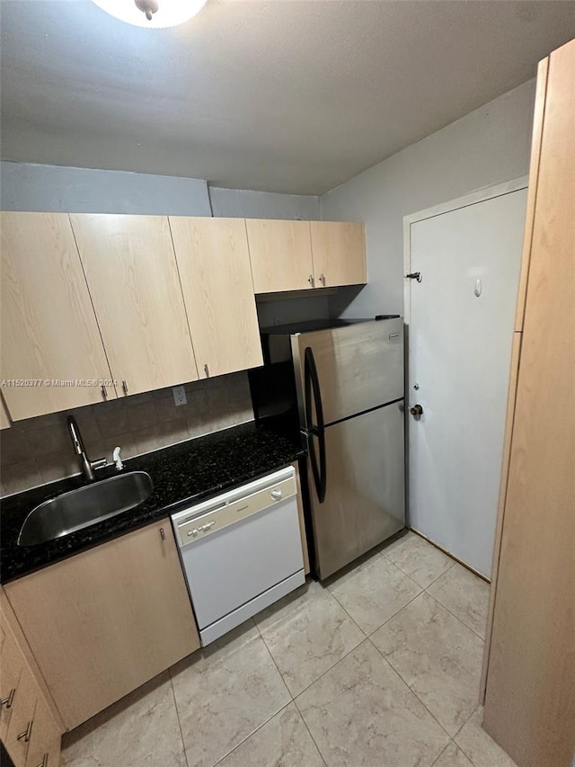 kitchen featuring dishwasher, dark stone counters, sink, stainless steel fridge, and light brown cabinetry