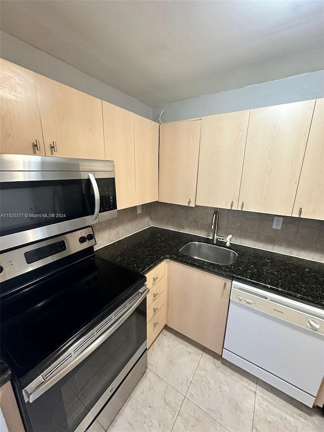 kitchen with light brown cabinets, dark stone counters, sink, light tile patterned floors, and stainless steel appliances