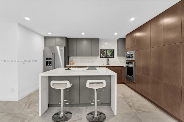 kitchen with a kitchen island, appliances with stainless steel finishes, a breakfast bar, sink, and light tile floors