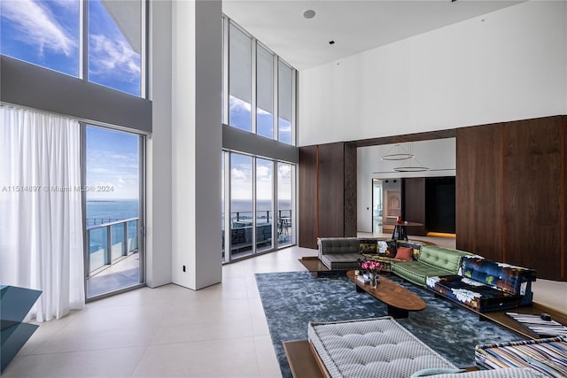 tiled living room with plenty of natural light, a water view, and a towering ceiling