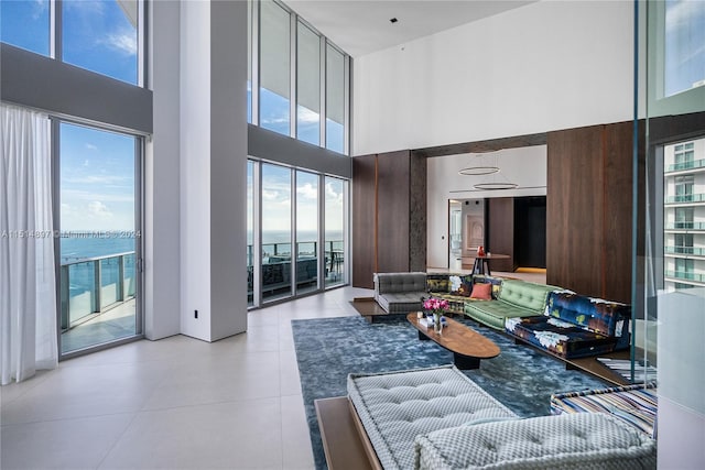 tiled living room featuring a high ceiling, a healthy amount of sunlight, and a water view