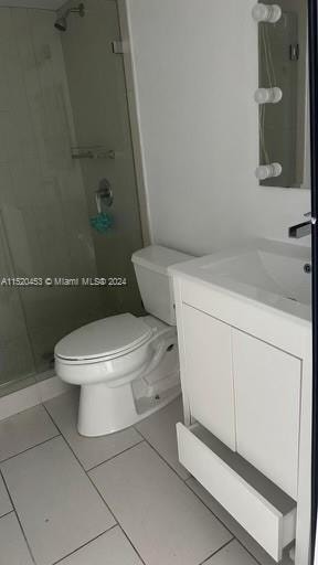 bathroom with tile floors, toilet, vanity, and a shower with shower door