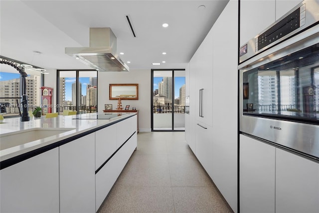 kitchen with double oven, black electric cooktop, white cabinets, and island range hood