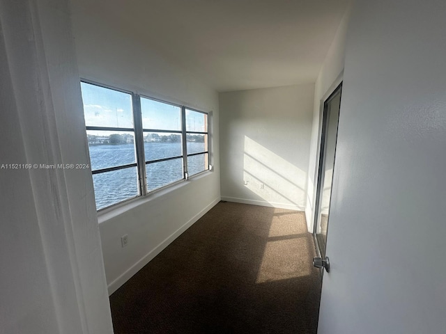 unfurnished room with a water view and dark colored carpet