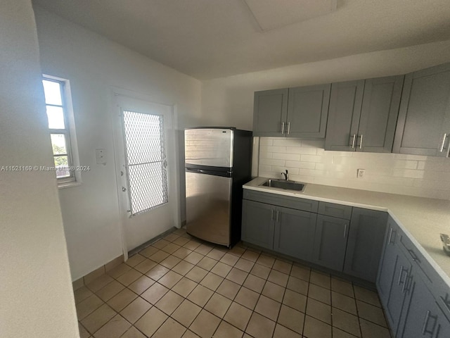 kitchen featuring sink, gray cabinets, light tile floors, stainless steel refrigerator, and tasteful backsplash