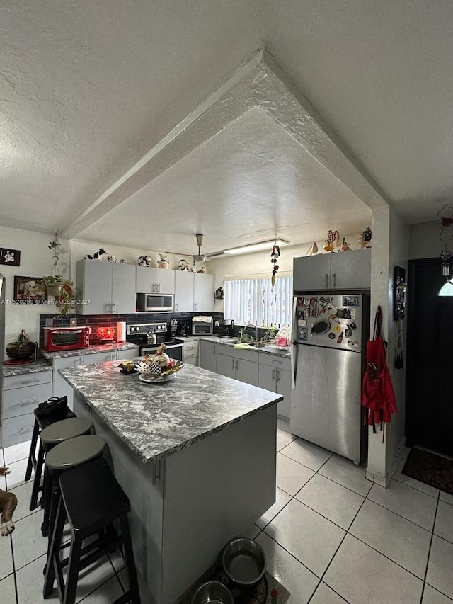 kitchen with appliances with stainless steel finishes, a textured ceiling, gray cabinetry, and light tile flooring