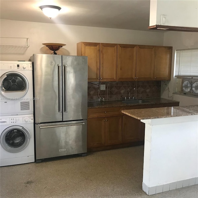 kitchen with light stone countertops, stainless steel fridge, tasteful backsplash, stacked washer and clothes dryer, and sink