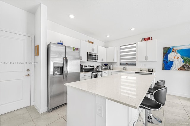 kitchen featuring white cabinets, appliances with stainless steel finishes, a kitchen island, light stone counters, and a breakfast bar area