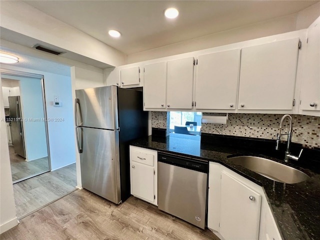 kitchen featuring backsplash, appliances with stainless steel finishes, sink, light wood-type flooring, and dark stone counters