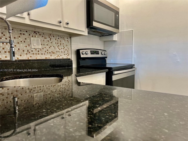 kitchen featuring sink, white cabinets, dark stone countertops, stainless steel appliances, and tasteful backsplash