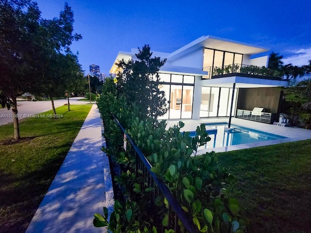 back of property with a balcony, a patio area, and a lawn