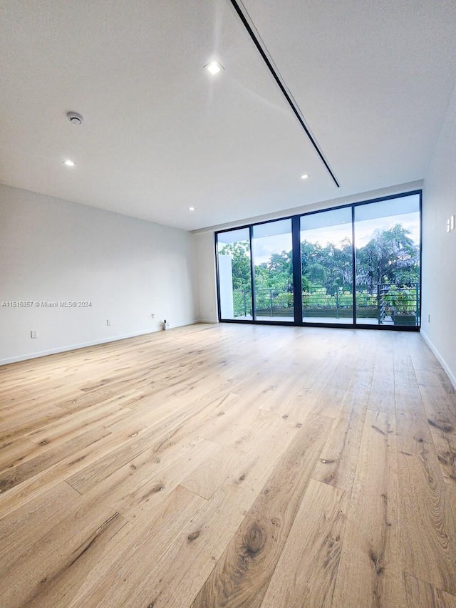 spare room featuring floor to ceiling windows and light hardwood / wood-style floors