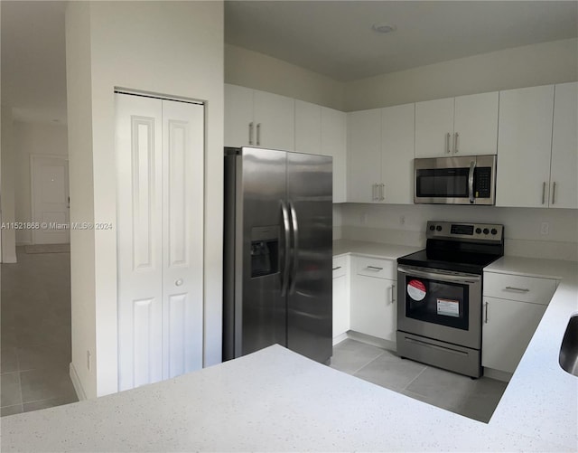 kitchen featuring light tile floors, appliances with stainless steel finishes, and white cabinetry