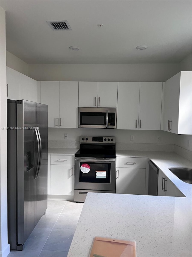 kitchen with stainless steel appliances, white cabinetry, light tile floors, and sink