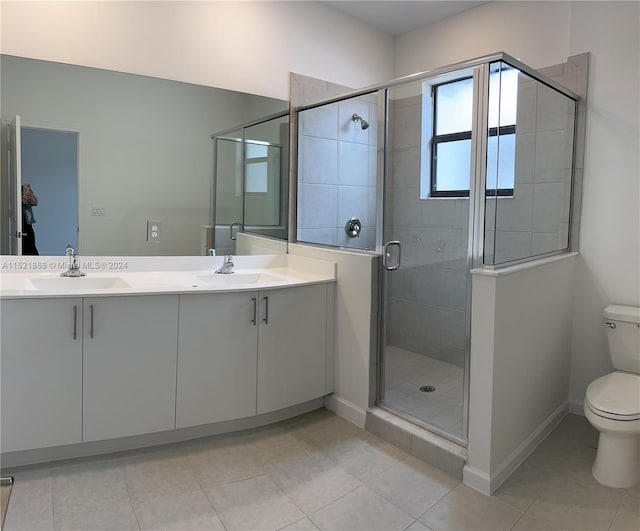 bathroom featuring toilet, tile floors, dual bowl vanity, and a shower with door