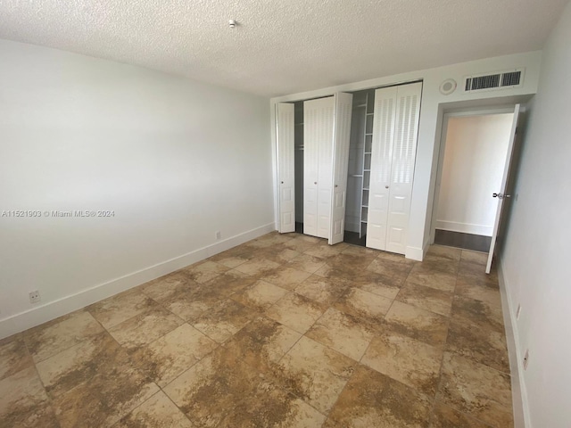 unfurnished bedroom featuring multiple closets, dark tile floors, and a textured ceiling