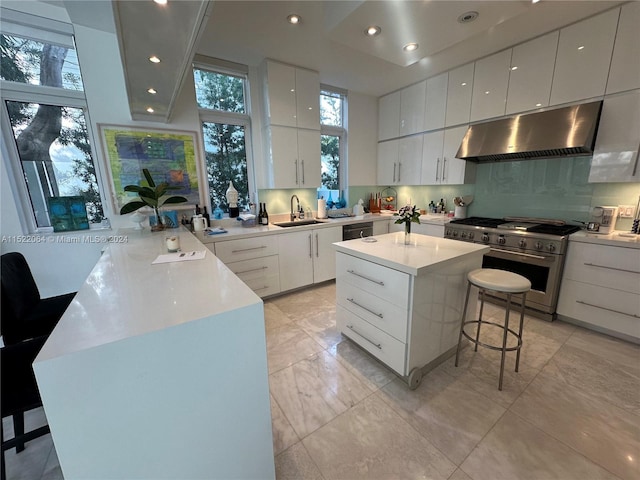 kitchen featuring stainless steel stove, wall chimney exhaust hood, a kitchen bar, white cabinetry, and a center island