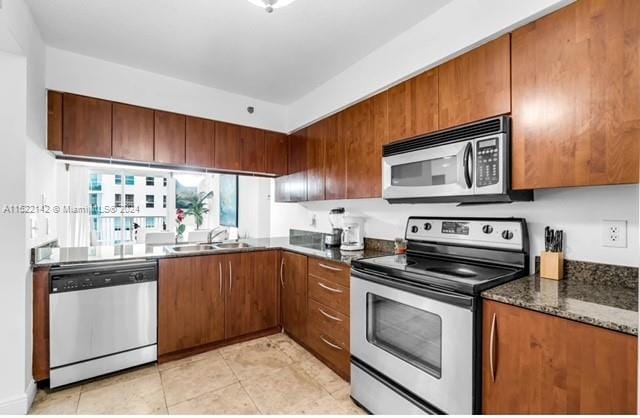 kitchen with dark stone counters, light tile floors, appliances with stainless steel finishes, and sink