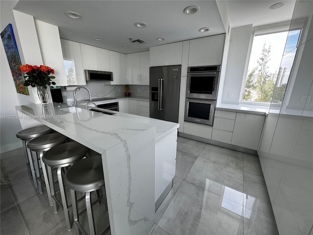 kitchen with stainless steel appliances, white cabinets, light tile floors, and light stone counters