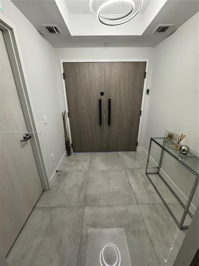 hall featuring a tray ceiling and light tile flooring